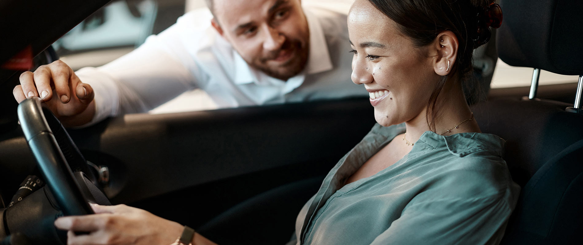 A woman behind the wheel of a car as a salesman looks through the window inside a dealership.